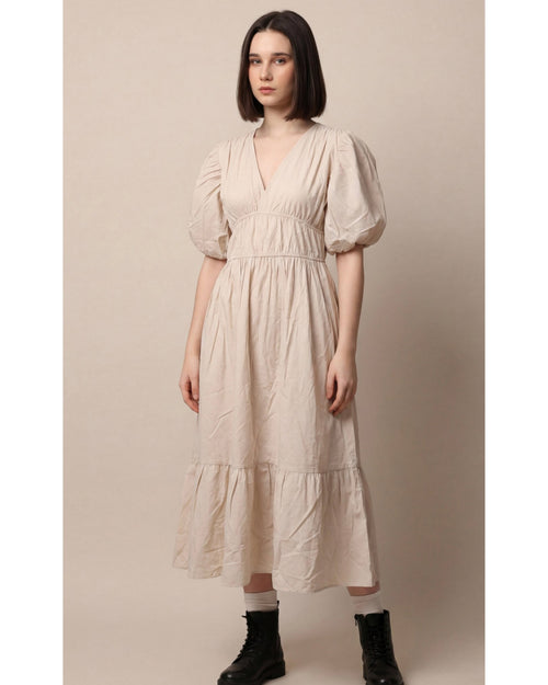 Woman wearing a beige dress with puffed sleeves against a plain background