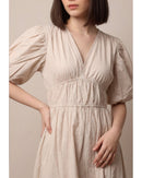 Woman wearing a beige dress with puffed sleeves against a neutral background