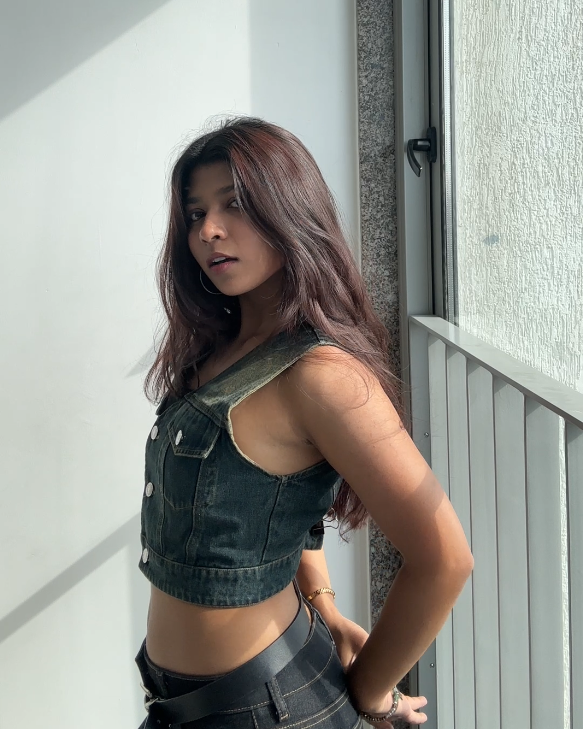 Woman standing on a balcony wearing a green crop top and black pants.