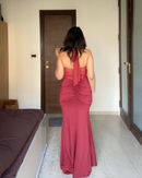 A woman viewed from behind wearing a floor-length dusty rose pink halter gown in a bedroom setting.